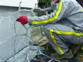 Pracownik w czerwonych rękawicach nakłada wzór na ścianę, tworząc imitację kamienia. To kluczowy etap izolacji przeciwwilgociowej.