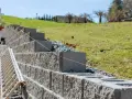 Budowa murek oporowy w ogrodzie. Betonowe bloki układane są warstwami, tworząc stabilną konstrukcję na zboczu.