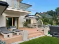 Nowoczesny taras z leżakami, stołem i krzesłami, wiszącym fotelem i jacuzzi. Idealne miejsce na relaks na świeżym powietrzu.