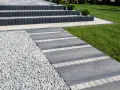 Nowy, tani chodnik przed domem z szarej płyty i białego gresu, obok żwiru i trawnika. Schody z ciemnego betonu.