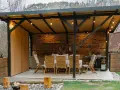 Nowoczesna budowa wiaty z miejscem do grillowania i jadalnią na świeżym powietrzu. Drewniane meble i ceglana ściana tworzą przytulną atmosferę.
