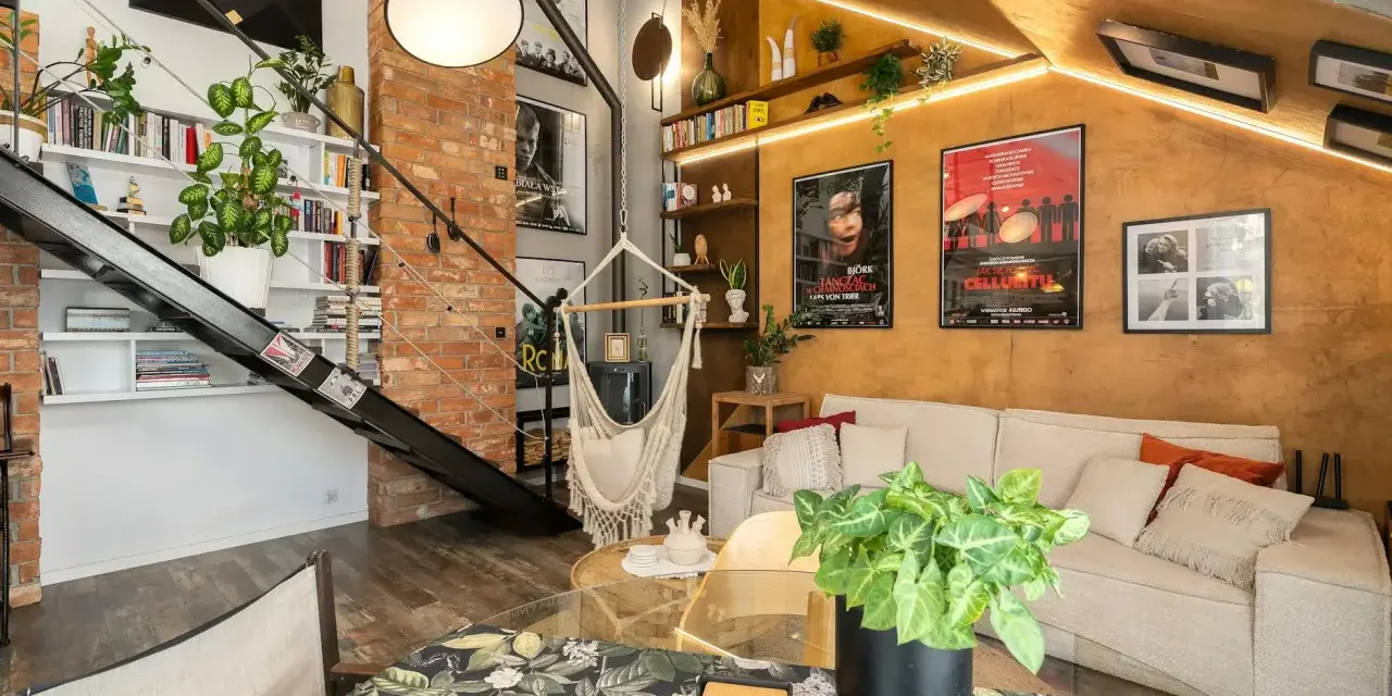 Wygodny salon w stylu loftowym z ceglaną ścianą, metalowymi schodami, wiszącym fotelem i dużą ilością zieleni.