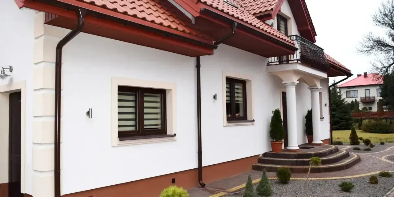 Elegancki cokół na elewacji domu, podkreślony brązowym tynkiem, harmonizuje z dachówką i stolarką okienną.