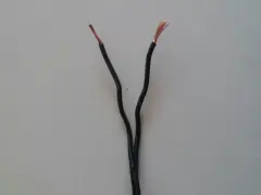 Dwa czarne przewody elektryczne rozchodzą się, odsłaniając miedziane końcówki. Czy czerwony to plus czy minus?