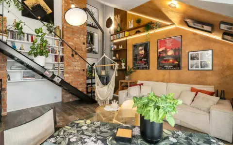 Wygodny salon w stylu loftowym z ceglaną ścianą, metalowymi schodami, wiszącym fotelem i dużą ilością zieleni.