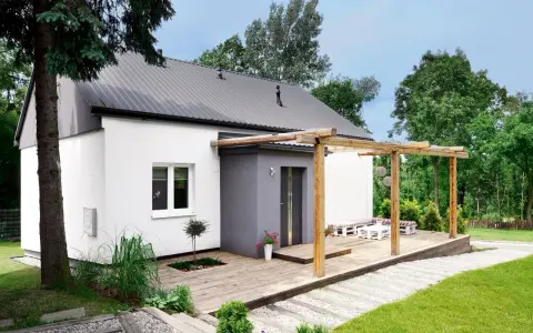 Drewniany taras z pergolą to świetny pomysł na taras przed domem. Urocze meble z palet i biały stolik zapraszają do relaksu.