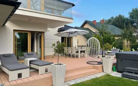 Nowoczesny taras z leżakami, stołem i krzesłami, wiszącym fotelem i jacuzzi. Idealne miejsce na relaks na świeżym powietrzu.