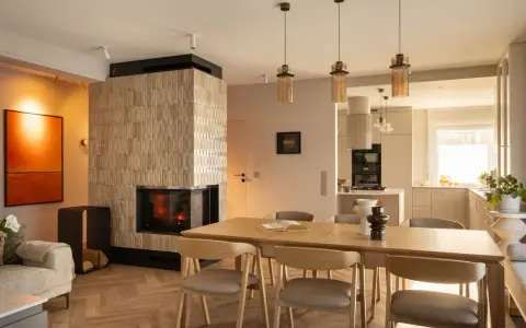 Przytulny salon z kominkiem i jadalnią w stylu klasycznym. Drewniany stół z krzesłami, kanapa i nowoczesny kominek tworzą ciepłą atmosferę.