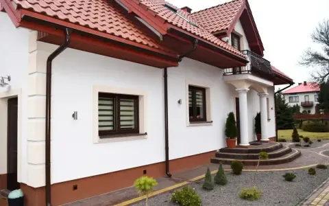 Elegancki cokół na elewacji domu, podkreślony brązowym tynkiem, harmonizuje z dachówką i stolarką okienną.