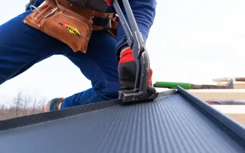 Pracownik montuje blachodachówkę, narzędzia i pasy robocizny dachu za m2.