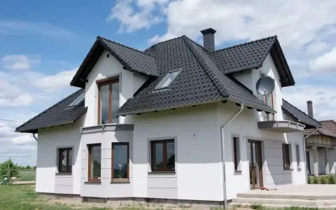 Nowoczesny dom z białymi boniami na elewacji, czarnym dachem i brązowymi oknami.