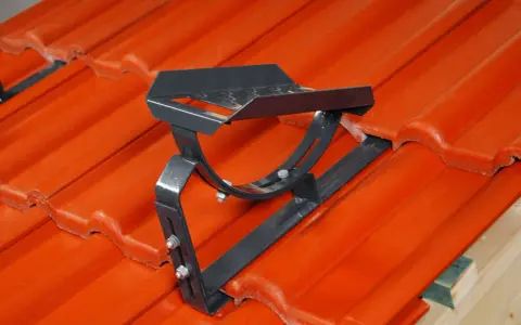 Metalowe stopnie kominiarskie zamontowane na pomarańczowej dachówce. Zapewniają bezpieczeństwo podczas prac na dachu.