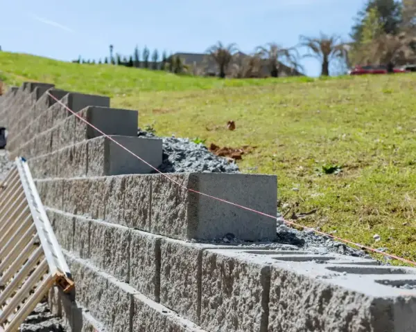 Budowa murek oporowy w ogrodzie. Betonowe bloki układane są warstwami, tworząc stabilną konstrukcję na zboczu.