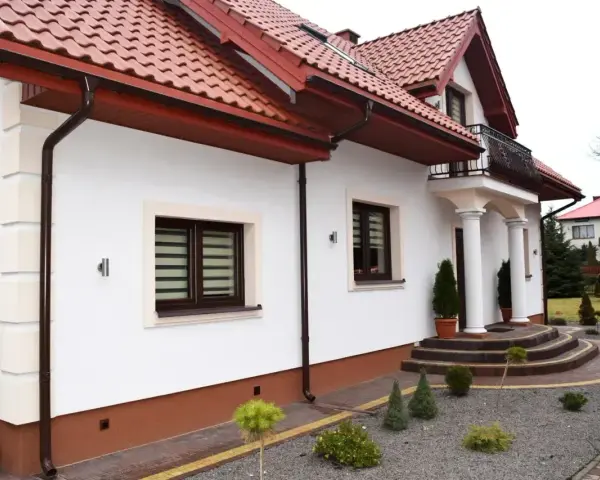 Elegancki cokół na elewacji domu, podkreślony brązowym tynkiem, harmonizuje z dachówką i stolarką okienną.
