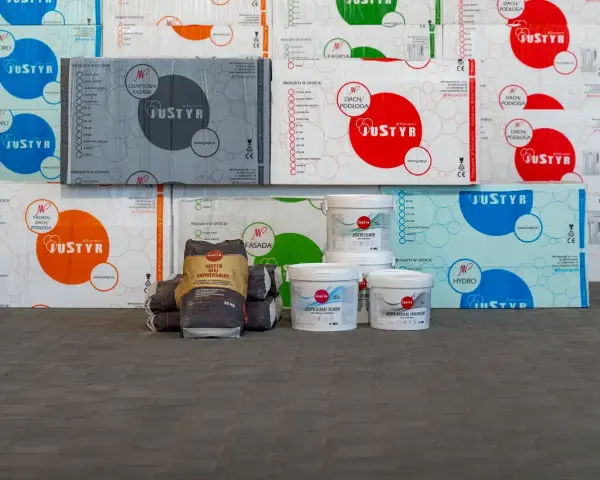 Stosy opakowań styropianu i wiader z produktami budowlanymi, w tym klej do styropianu Justyr.