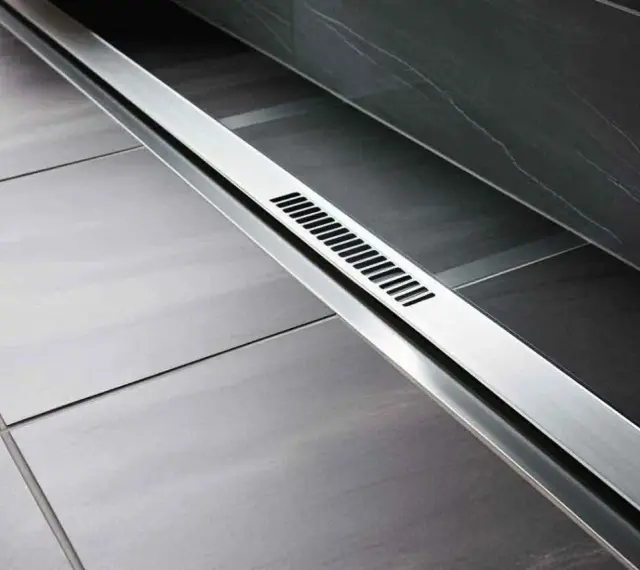 Nowoczesny, liniowy wpust prysznicowy ze stali nierdzewnej w łazience z szarymi płytkami.
