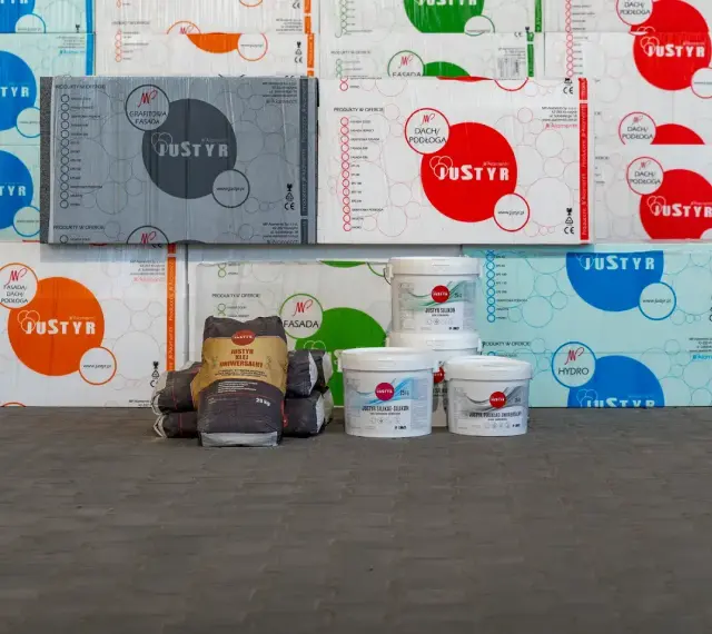 Stosy opakowań styropianu i wiader z produktami budowlanymi, w tym klej do styropianu Justyr.