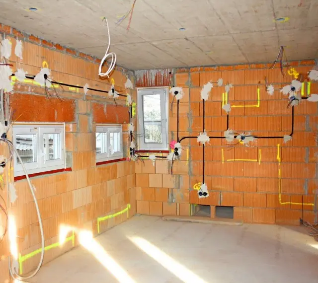 Rozpoczyna się instalacja elektryczna w domu. Widoczne przewody, puszki i oznaczenia na ceglanych ścianach.