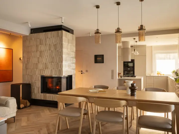 Przytulny salon z kominkiem i jadalnią w stylu klasycznym. Drewniany stół z krzesłami, kanapa i nowoczesny kominek tworzą ciepłą atmosferę.