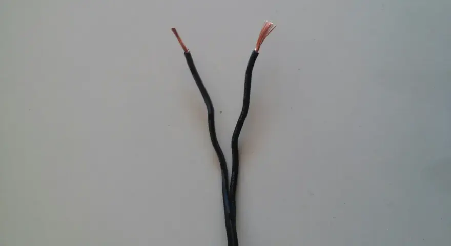 Dwa czarne przewody elektryczne rozchodzą się, odsłaniając miedziane końcówki. Czy czerwony to plus czy minus?