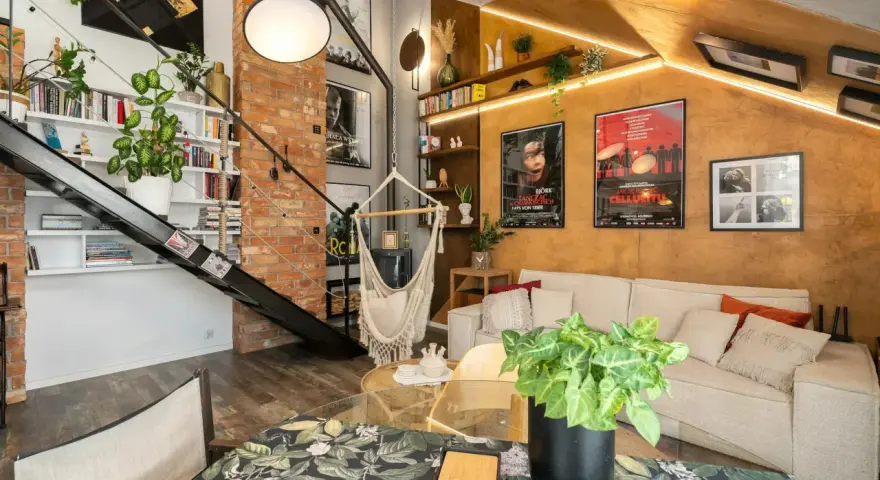 Wygodny salon w stylu loftowym z ceglaną ścianą, metalowymi schodami, wiszącym fotelem i dużą ilością zieleni.