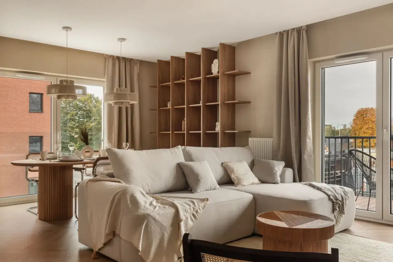 Przytulny salon w domu z jasną sofą, drewnianą biblioteczką i jadalnią przy oknie.