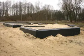 Izolacja starych fundamentów z kamienia w trakcie budowy. Czarna folia zabezpiecza ściany przed wilgocią.