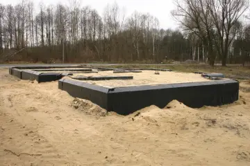 Izolacja starych fundamentów z kamienia w trakcie budowy. Czarna folia zabezpiecza ściany przed wilgocią.